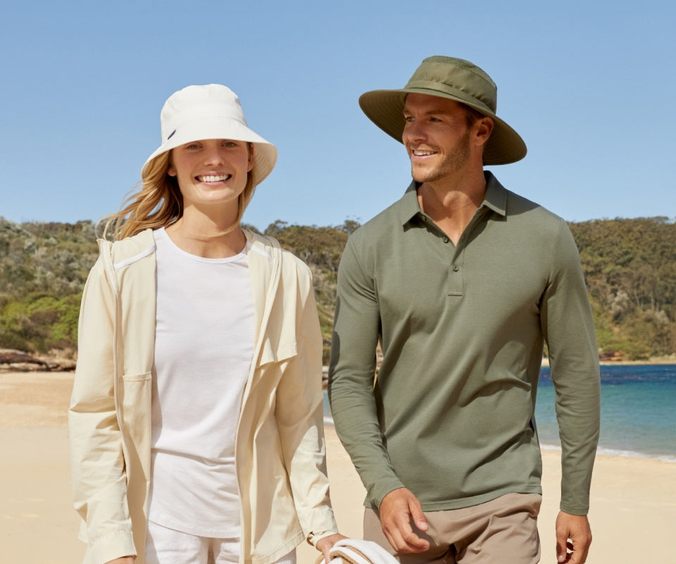 Two people on a beach wearing hats and casual clothing.