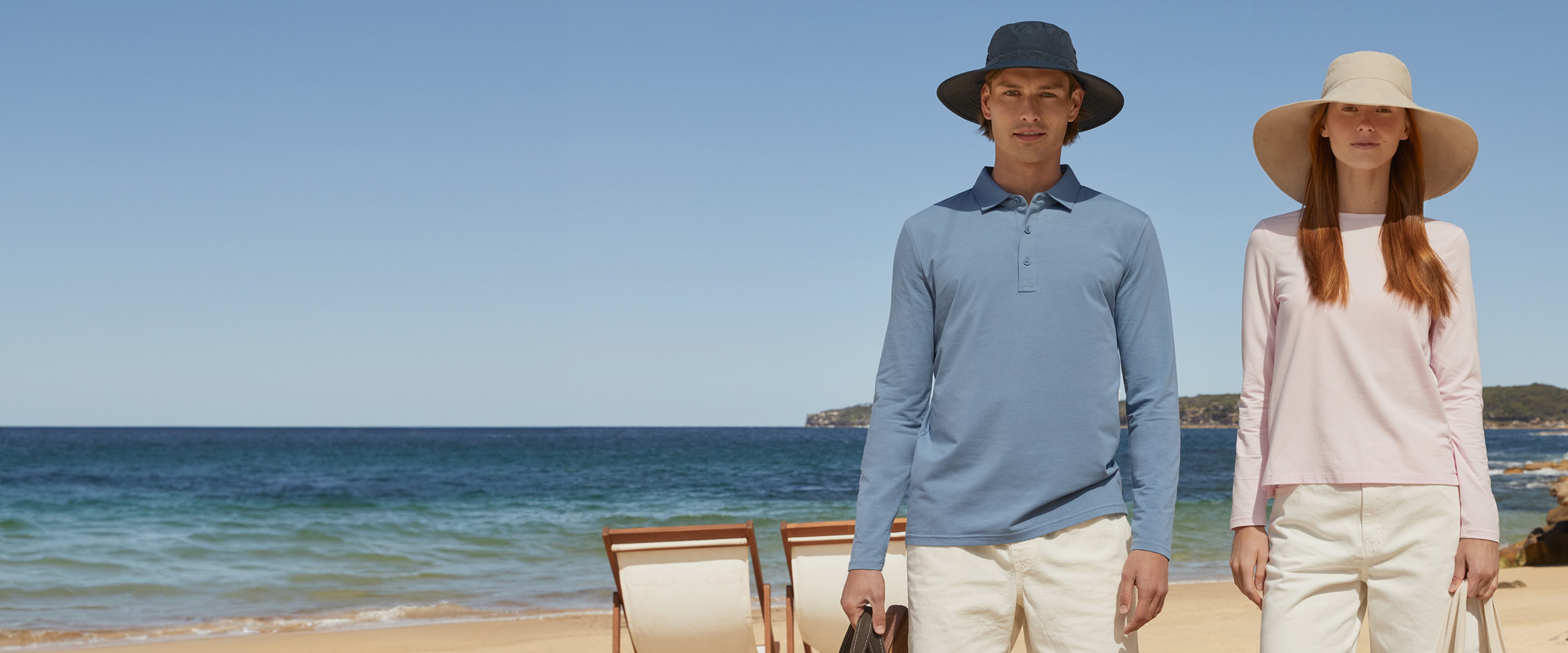 Two people standing on a beach with clear blue sky and ocean.
