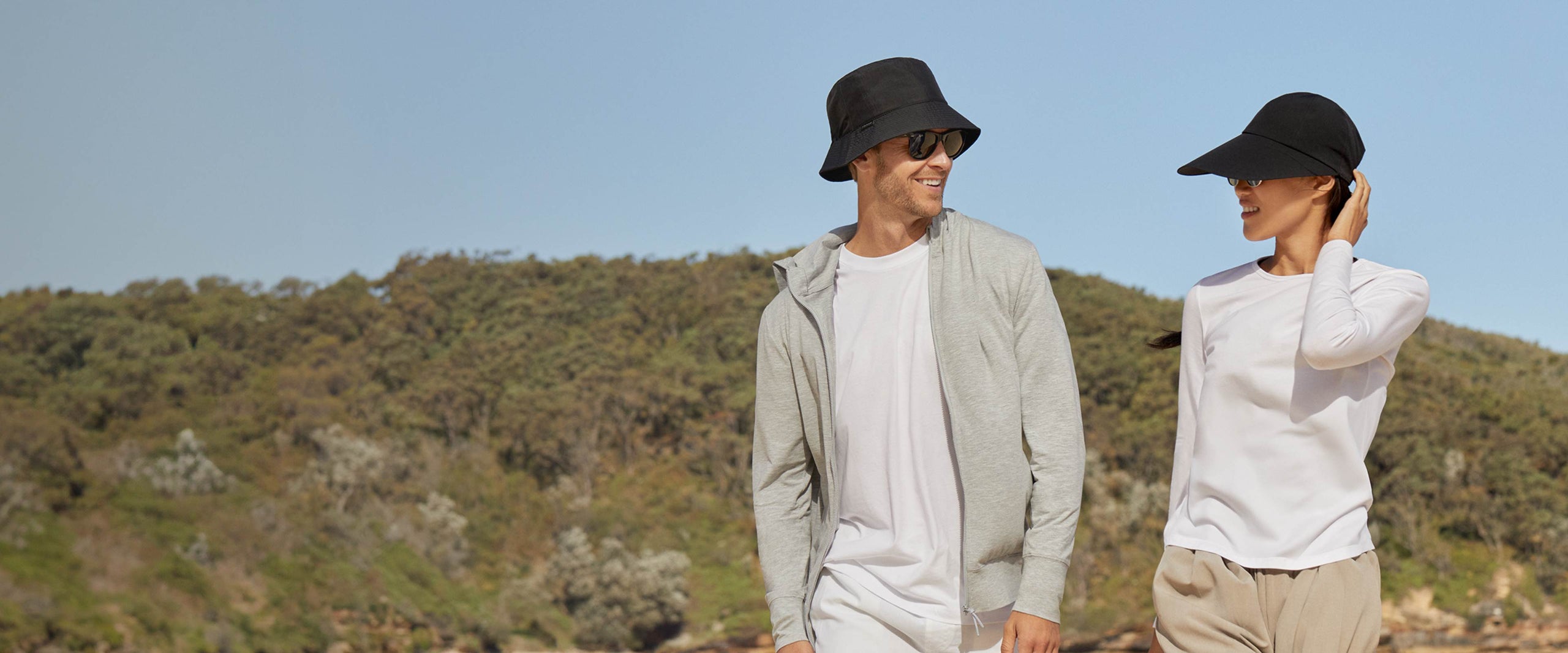 Two people wearing hats in a scenic outdoor setting with mountains in the background.