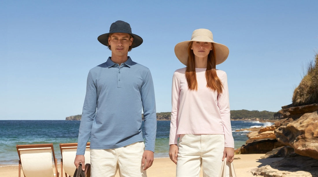 A man and a woman on a beach wearing sun smart clothing and sun hats.