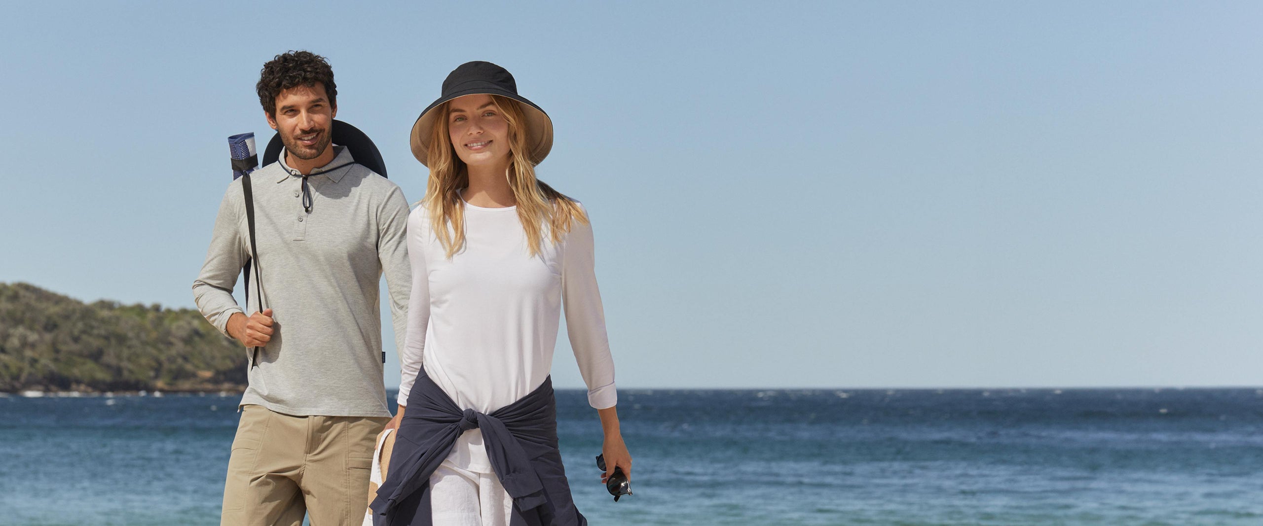 Two people walking on a beach with clear blue sky and ocean in the background