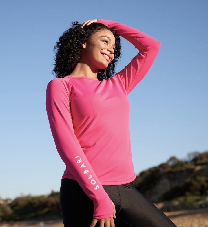 Woman wearing a pink long-sleeve rash guard with 'SOLBARI' on the arm, a clear day.