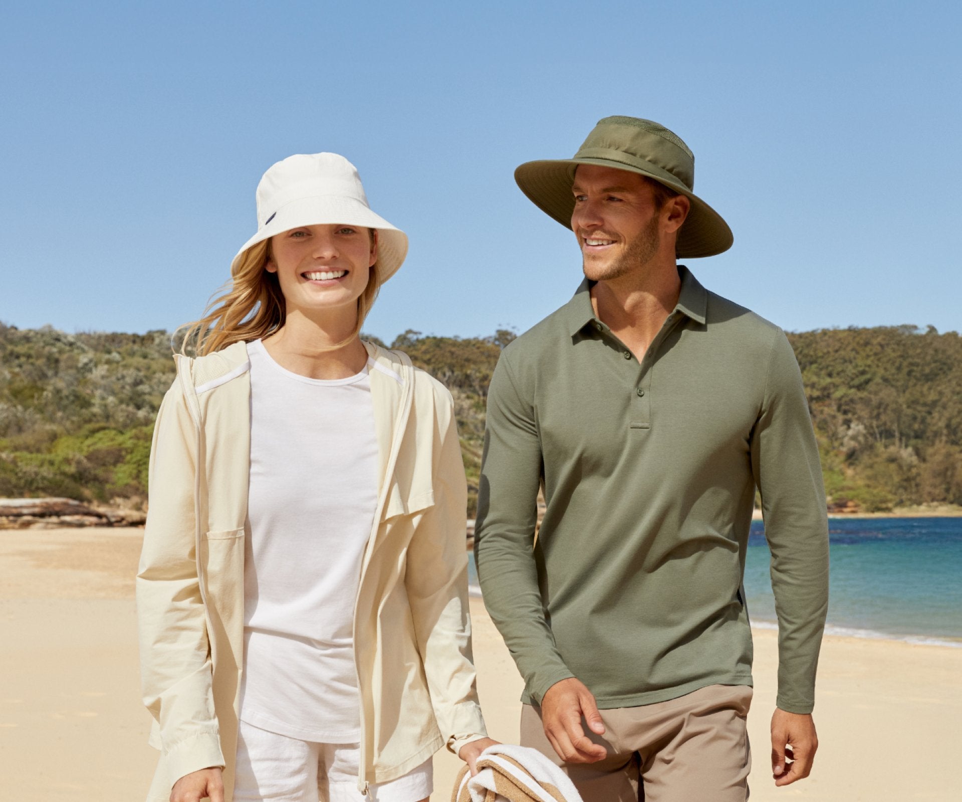 Man and woman walking on a beach with a clear blue sky and ocean in the background.