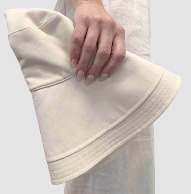 White bucket hat held by a hand on a light gray background